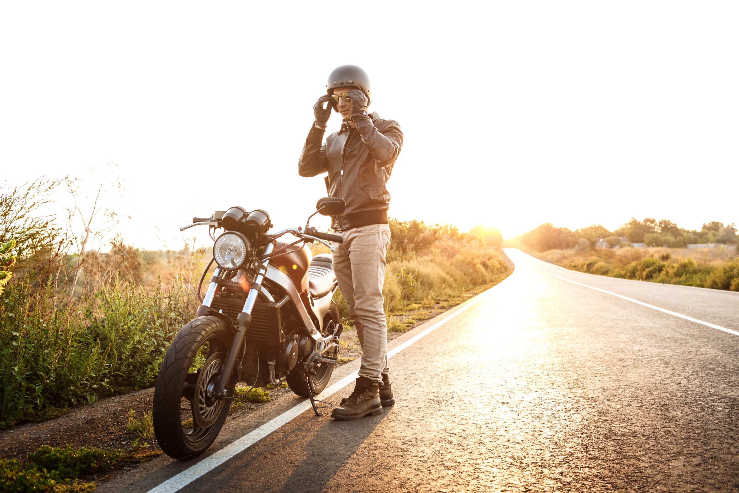 Young handsome man in leather jacket posing near his motorbike at countryside road.